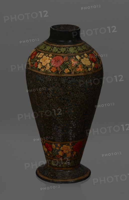 Vase, Qajar dynasty 1785–1925, Persian, Islamic art; lacquer vase, 19th century, Iran; vessel, height 32.0 cm, diameter 17.0 cm. Decoration: densely placed plant motifs peonies with gold contouring; on the collar and above the foot flowers red and gold. Inside a card no. 54 with an inscription in Italian noting it is a lacquer vase., The image shows a tall ceramic vase with a narrow neck and flared base, decorated with floral bands and patterns. The upper rim and neck are dark, almost black, while a band near the shoulder features painted flowers in red, yellow, orange, and green against a darker background. The main body has a dark, textured surface with subtle floral motifs in deep blue and muted green tones with small highlights of yellow. A lower band near the base repeats the colorful floral motif with reds, yellows, oranges, and greens, and the base itself is dark with decorative patterns and a thin lighter edge. The overall color palette includes black, dark blue, green, red, ye...