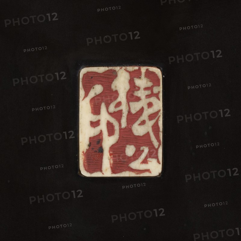Panel, Japanese, Meiji 1868–1912, 19th/20th century, sculpture; height 75.0 cm, width 42.0 cm, depth 3.0 cm. Depicts boys/children with toads/frogs among rocks; carved with asanoha and shippo patterns. Unknown creator; ., A rectangular off-white plaque with rounded corners sits centered on a dark black background; the plaque shows a pattern of irregular red shapes and areas of off-white where the base color shows through, with some subtle dark specks and faint horizontal striations in parts of the red, and the edges of the plaque have slight discoloration and shadowing against the black.