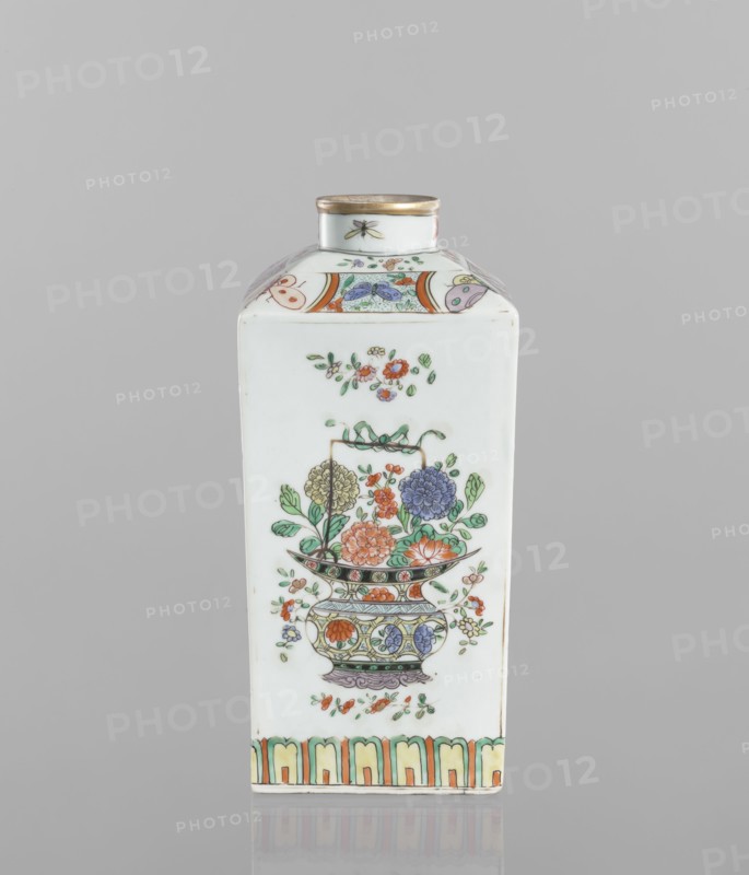 Bottle; decorated colored porcelain vessel, 18th century, China. Decorated on each side with a basket of peonies, four flower sprigs and a trail of lotus petals at the base of the belly; on the shoulders with butterflies, trellises with flower rosettes and sprigs with flowers; on the neck with four insects. Height 25.3 cm; width 10.8 cm; depth 10.8 cm. Subjects: peonies, butterflies, insects, floral decorations., A rectangular white porcelain bottle with a short cylindrical neck and a gold rim features a painted floral arrangement on its front face, showing a decorative vase filled with a group of flowers including blooms in orange, purple, yellow, and blue with green leaves and small scattered blossoms; the shoulder area has bands of patterned panels in orange, green, purple, and blue, and a small insect motif on the neck; the base edge is accented with a repeating arch pattern in green, orange, and yellow, all set against a light gray background.