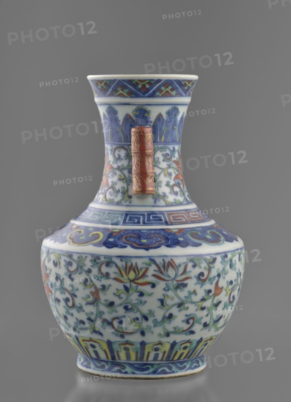 Vase with threads in the shape of bamboo twigs; maker, Chinese; Qing dynasty 1644–1911, Qianlong period 1736–1795; colored porcelain; plant motifs including lotus tendril ornament and artemisia leaves; decoration: lotus tendril on the belly, lambrequin ornament on the shoulders, geometric and plant borders on the neck; vessel; height 20 cm, diameter 14.5 cm, weight 0.8 kg., A ceramic vase with a bulbous body and a flared neck stands against a gray background, decorated with intricate floral and foliate patterns in blue, green, red, yellow, and white; the neck and shoulder feature bands of geometric and stylized motifs in blue and red with accents of green and yellow, and a raised rectangular handle in a reddish-brown color with gold detailing is attached to the neck; the main body shows scrolling vines and lotus-like flowers in shades of blue, green, red, and yellow on a white ground, with additional blue and yellow decorative bands near the base and rim.