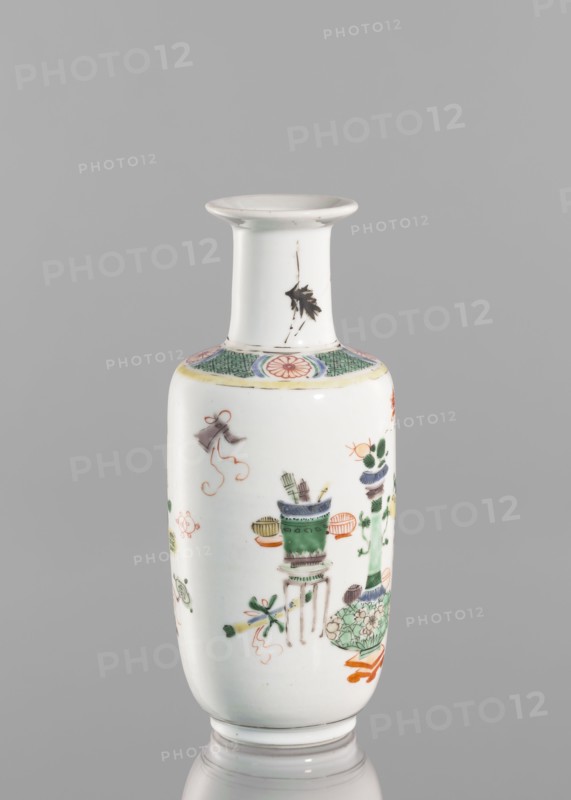 Vase, Chinese, Qing dynasty 1644–1911, 19th century. Colored porcelain vessel decorated with bai gu hundred antiquities ornament. Height 20.8 cm; diameter 7.5 cm., A slender porcelain vase with a flared rim and narrow neck sits against a plain gray background; the vase is predominantly white with painted decorations in green, orange, black, pink, yellow, and blue, including floral motifs, stylized leaves, and objects arranged around the body, a decorative band with green crosshatch and pink circular motifs near the shoulder, and a small black leaf-like mark on the neck.