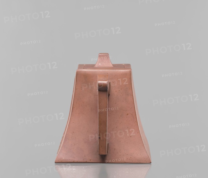 Teapot with a lid, tea vessel, Yixing-style red-brown stoneware, inscriptions, Chinese, Qing dynasty 1644–1911, 19th century, Harbin China, height 12.2 cm, width 16.3 cm, A triangular-shaped object with a handle facing forward sits on a reflective surface; the object is a warm reddish-brown with small darker speckles and subtle variations in tone, and it casts a soft reflection. The background is a smooth, light gray that fills the frame. The handle and top section share the same reddish-brown color, and the object shows slight surface texture and tiny imperfections.