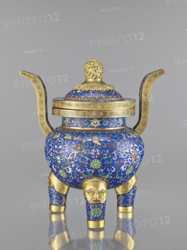 Ding-type incense burner with cover, cloisonné enamel, Qing dynasty 1644–1911, 19th century, China; decorated with bats, dragons, leiwen and meander ornament, plant motifs; vessel; height 38.5 cm, width 34.5 cm., An ornate vessel with a domed lid and two upward-curving handles sits on a reflective surface, decorated primarily in rich blue with intricate swirling floral and vine patterns in green, white, red, and gold; the lid and rim feature gold bands with geometric motifs and a pierced gold finial, while the body rests on three short legs covered in the same blue and floral enamel, each leg topped by a gold lion-like mask and finished with gold bands at the feet.