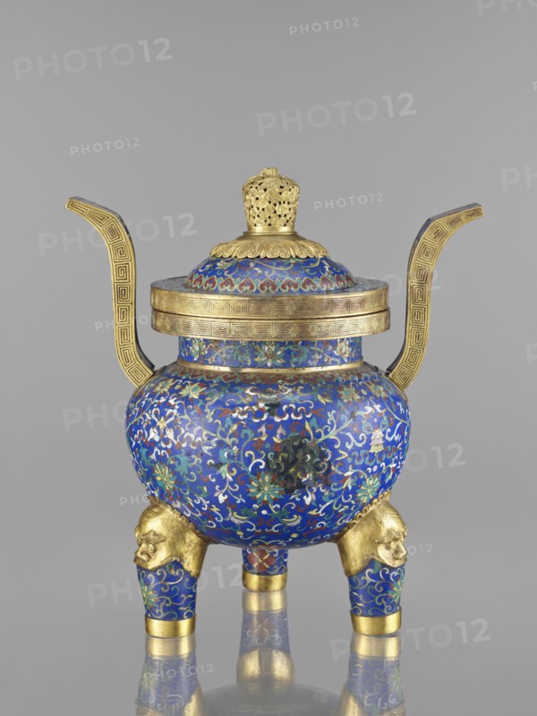 Ding-type incense burner with cover; cloisonné enamel; Qing dynasty 1644–1911, 19th century, China; decorated with bats and dragons, leiwen and meander ornament; vessel; height 38.5 cm, width 34.5 cm., A decorative vessel with a rounded body and a domed lid sits on a reflective surface; the body and lid are covered in intricate enamel patterns dominated by deep blue with accents of turquoise, green, red, white, and gold; two tall, curved handles extend from the sides in a metallic gold with geometric border motifs; the lid has a gold finial with pierced openwork and a scalloped gold rim; the vessel rests on a group of three short legs that are blue with gold floral patterns and topped with sculpted gold animal heads; a broad gold band encircles the rim of the body, and additional gold bands accent the leg ends, creating a contrast with the richly colored enamel decoration.