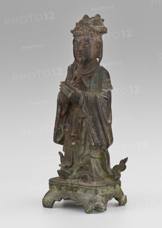 Dignitary - official, unknown,  craftsman author, figurine of a man, Chinese art, Chinese culture, Qing 1644–1911, scholars, sages, government officials, 19th century, China, sculpture; height 28.5 cm, width 12.4 cm, depth 8.7 cm, A standing statue of a robed figure with hands held together at chest level, wearing an ornate headdress and layered garments with detailed patterns; the figure has a calm facial expression and a long beard. The sculpture rests on an ornate base with curved legs and decorative motifs, and there are flowing drapery elements and small curved extensions around the lower robes. The visible colors include dark brown, green patina, and hints of reddish-brown.