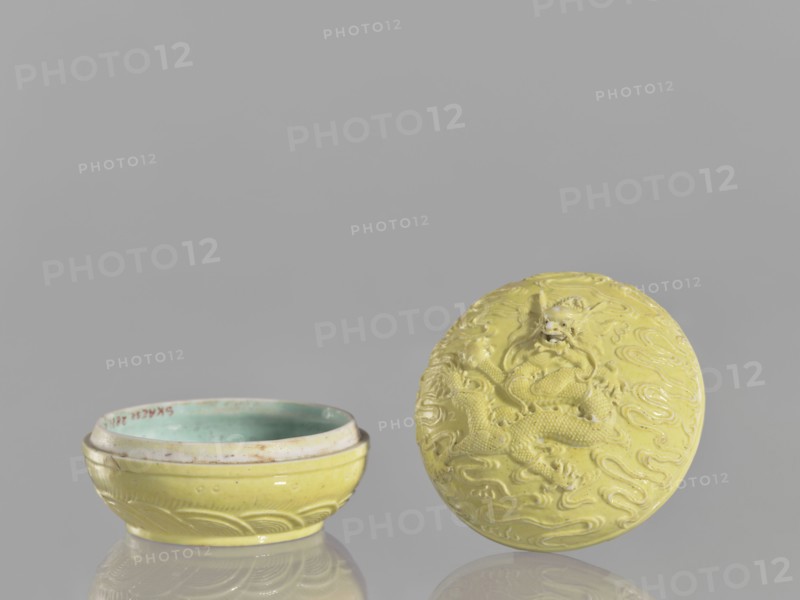 Box with a lid, Kangxi style, ceramics, boxes, Qing style, dragons iconography, Chinese art, Chinese culture, pearls, clouds, Qing 1644–1911, Kangxi 1662–1722, 18th century, China, vessel, height 5 cm, diameter 7.4 cm, A shallow round bowl and its separate lid sit on a reflective surface against a plain gray background; both pieces are primarily yellow with a glossy finish, the bowl interior showing a greenish-blue glaze, and the lid displaying a raised dragon design with flowing cloud-like patterns in the same yellow tone.