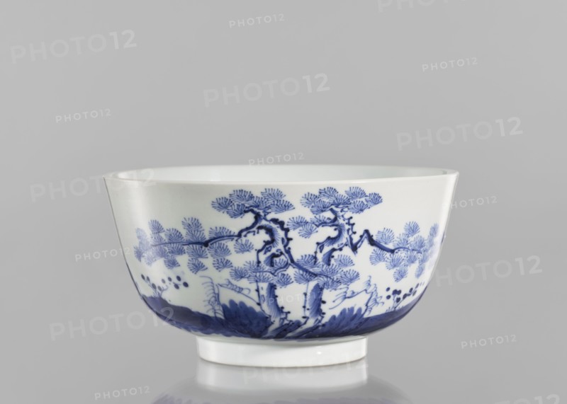 Bowl, ceramics, blue and white porcelain, inscriptions, landscape motifs, fishermen; Chinese, Qing 1644–1911, 19th century, South China; vessel, height 8.8 cm, diameter 17 cm. Inscriptions: ?? Wèi Shui, the Wei River, ??? tóu gan rì, the day of casting the fishing rod, ?? Qí Shan, Mount Qi, ??? rù mèng chén, entering a dream in the morning — verse evoking a peaceful or nostalgic scene of fishing by the Wei River and Mount Qi., A white ceramic bowl with a glossy surface sits against a gray background, decorated around its exterior with a blue painted landscape motif showing stylized trees with textured foliage, winding branches, and ground vegetation, with darker blue shading along the lower rim and a white foot at the base.