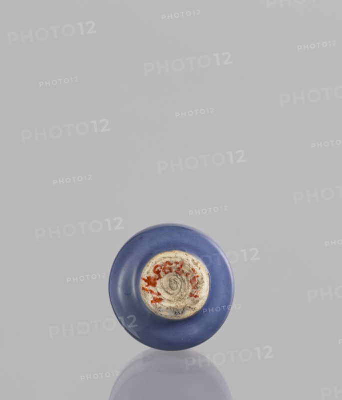 Bottle, Chinese, ceramics, poudre bleu, 19th century, China, vessel, height 5.3 cm, A single round object with a smooth blue outer surface sits near the bottom center of the image against a light gray background, showing a worn circular central area with a rougher texture and patches of reddish and beige tones; a subtle reflection of the object appears beneath it on the surface.