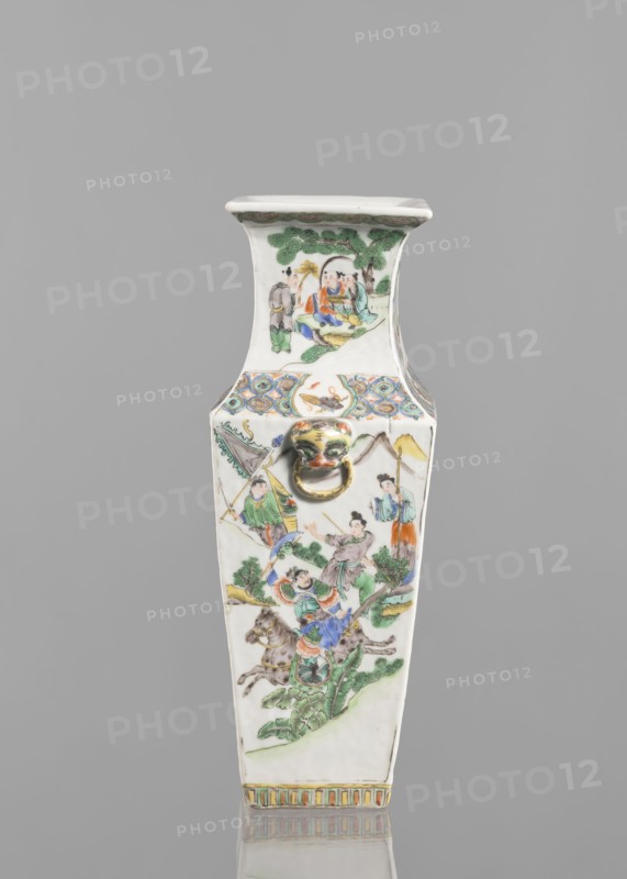 Vase, Chinese, 18th century, painted colored porcelain, height 31.2 cm, width 11.0 cm; figurative genre scenes depicting battles., A tall, narrow porcelain vase with a tapered square shape is shown against a plain gray background, decorated with painted scenes of figures, trees, and landscapes in colors including green, blue, orange, yellow, red, brown, and black, and featuring a small sculpted lion head with a gold-colored ring on the front; the top rim and neck area show a painted tree scene, the main body displays several groups of people in traditional dress and horses amid foliage and hills, and the base has a band of vertical decorative stripes in muted colors.
