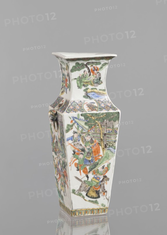 Vase, Chinese, Chinese art, figurative scenes, battle scenes, ceramics, colored porcelain, genre scenes, battles, 18th century, China, vessel, height 31.0 cm, width 11.0 cm, A tall, tapered ceramic vase with a flared square mouth and a square base, decorated on its white surface with painted figurative scenes and ornamental bands; visible colors include green, orange, blue, yellow, brown, black, and pale pink, with gold or tan accents. The main body shows a group of figures in traditional dress beneath trees and near architectural elements, with flowing garments in green, orange, blue, and yellow and faces rendered in pale tones; one side shows figures riding an animal and others carrying banners or weapons. The neck of the vase displays a scene of seated figures beneath stylized trees, while the shoulder area features a band of circular and floral motifs in blue, green, and orange. The vase has a decorative ring handle on one corner and a striped geometric border at the base in yellow...