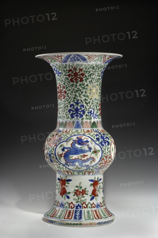 Zun-type vase decorated with images of dragons; dragons, dragon with pearl, plant twigs ornament; Chinese art, Chinese culture; Qing style; ceramics, colored porcelain; wucai/famille verte decorative technique overglaze enamels and underglaze cobalt; developed in Ming, popular in Qing; five-toed dragons playing with a fiery pearl imperial emblem; symbolizing rain, abundance, prosperity; 18th/19th century, China; vessel; height 40.6 cm, diameter 21.5 cm., A tall porcelain vase with a flared rim and bulbous midsection standing on a slightly flared foot, decorated all over with intricate painted patterns in blue, green, red, and yellow; the neck and upper body feature scrolling green vine motifs with stylized floral forms in red, blue, and yellow, while the bulbous section shows a blue dragon motif surrounded by decorative cloud and scroll panels in red, green, and blue; the lower section has floral sprays in red and green with blue accents and a band of repeating leaf and geometric patte...