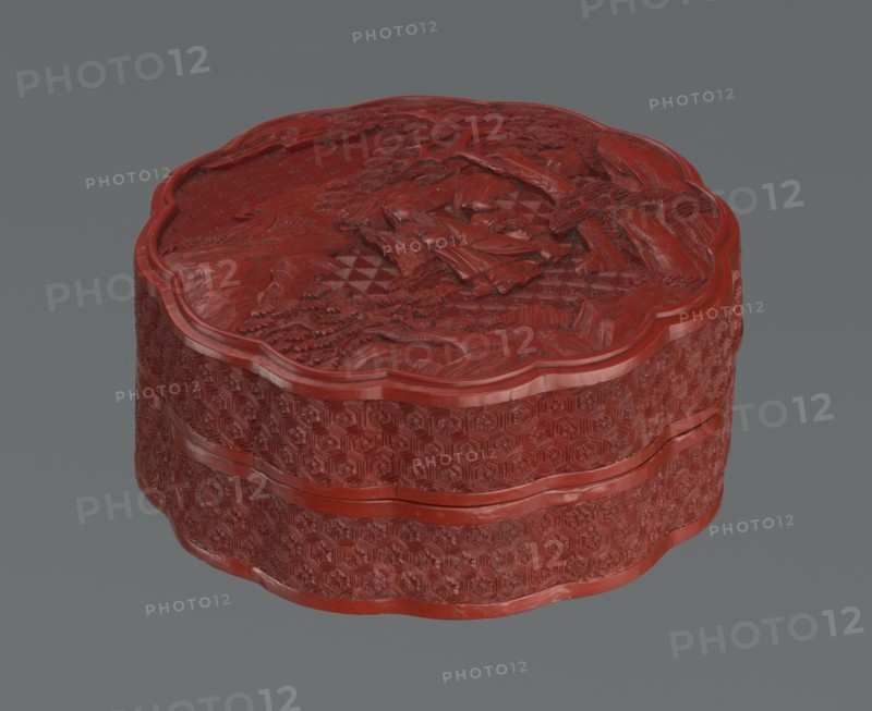 Box with a lid, Chinese, Qing dynasty 1644–1911, 2nd half of the 18th century. Lacquered box with figurative scenes of sages, scholars and servants amid landscape motifs pine trees, rocks, rosettes, kikko tortoiseshell pattern, geometric ornament. Vessel. Height 11.0 cm; width 4.8 cm., The image shows a carved, round box with a scalloped edge, rendered in a deep red color against a gray background; the box has intricate raised floral and geometric patterns on its sides and a detailed relief scene on its lid, with visible texture and highlights in red and darker red tones.