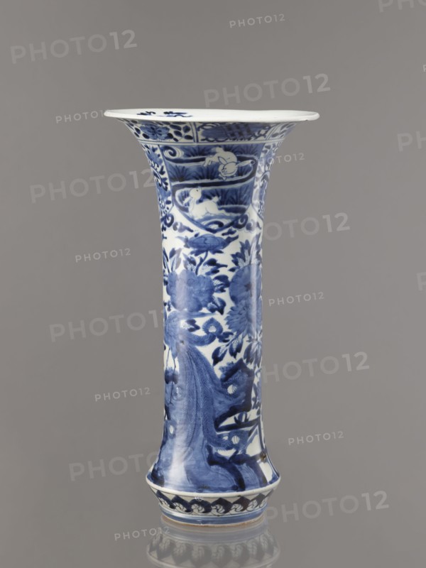 Vase, Japanese, Edo period 1603–1868, Genroku–Kyoho ca. 1690–1730, Arita; blue-and-white porcelain vessel, height 39.0 cm, diameter 20.3 cm; decorated with hares/rabbits, peonies, lotuses, phoenix hoo, kacho flowers-and-birds iconography. One of four elements of a set., A tall flared ceramic vase with blue painted floral and decorative motifs on a white ground, showing a group of stylized flowers and leaves and a few curved decorative bands, standing against a plain gray background.