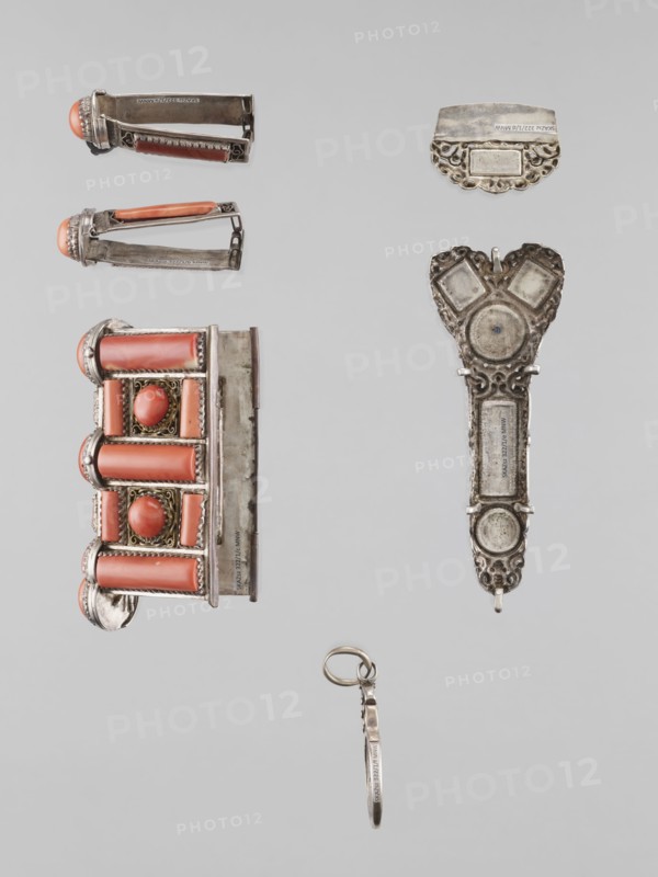 Braid ornament, braid ornament jewelry, artistic crafts; braid ornament, braids, women's ornament; 19th–20th century, Mongolia; jewelry; height 3.0 cm, width 7.8 cm, A collection of small metal objects arranged on a pale gray background, including a decorative rectangular piece with cylindrical coral-colored elements and oval coral cabochons set in ornate silver frames, a pair of hinge-like metal clips each with a coral-colored rounded end and silver filigree, an elongated ornate silver pendant with circular and heart-shaped motifs and decorative openwork, a small curved silver plate with scalloped edge and filigree details, and a thin silver ring attached to a narrow metal band; visible colors include silver, coral, gray, and a hint of gold in the filigree.