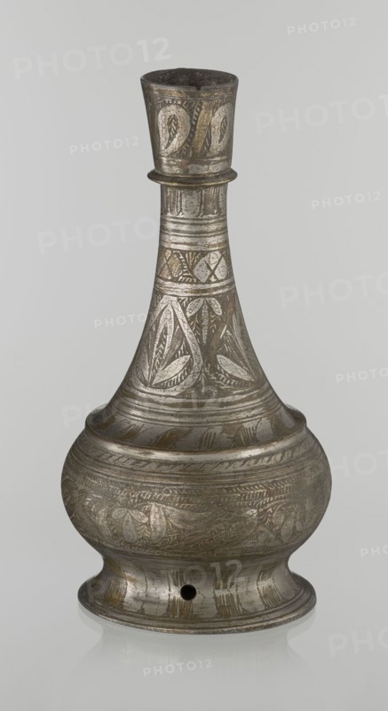 Bottle, Islamic art, Arabic, geometric ornament, plant motifs; neck slender toward the top ending with a straight spout; engraved patterns painted with golden-brown paint; early 20th century, Middle East; vessel; height 21.6 cm, width 10.5 cm., An antique metal vessel with a narrow neck and bulbous body sits against a plain light gray background; the surface shows engraved decorative patterns including leaf-like motifs and bands of etched lines, with areas of darker tarnish and lighter silver highlights giving overall colors of gray, silver, and muted brownish tones; the vessel has a flared rim, a rounded base with a small round hole, and an overall aged, slightly reflective finish.