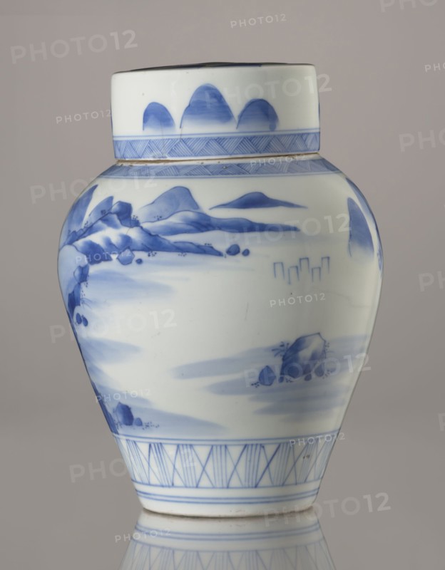 Storage vessel with lid by Zôshuntei Sanpô signature painted underglaze in cobalt: Zoshuntei Sampo zo, c. 1842–1878. Pear-shaped blue-and-white porcelain storage pot with flat cylindrical lid; height 21.8 cm, diameter 15.3 cm; Arita, Japan. Decorated in a Chinese-style Southern School landscape: an old man resting alone under a pine on a rocky cliff overlooking a wide body of water, with mountainous scenery, a waterfall, lofty peaks, and distant boat sails. Lower base bears a wide ornamental band of three vertical and two crossed lines; neck and lower edge of lid show diagonal-line bands forming triangular motifs; lid decorated with a rock motif. Design reflects influence of Chinese painting and the Japanese bunjinga nanga movement; free-form painting with precise, masterful cobalt lines in bright, pure shades. Subject motifs: pines, mountains, waterfalls, sages; classification: storage pot; period: late Edo–Meiji Edo 1603–1868; Meiji 1868–1912., A white ceramic jar with blue painted d...