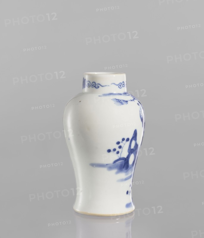 Meiping vase, meiping vessel type, ceramics, blue and white porcelain with figural scenes and park/landscape motifs, Qing dynasty style 1644–1911, baluster-shaped with a belly narrowing at the bottom and flaring toward the foot, narrow neck, 19th century, China, height 12.5 cm, diameter 7.8 cm., A small ceramic vase with a rounded shoulder and slightly flared base sits against a plain light gray background; the vase is glossy white with delicate blue painted decoration including a band of cloudlike scrolls near the short neck and a few brushworked motifs and dots on the body, with visible blue brushstrokes suggesting organic shapes; the rim and base edges show a faint warm beige tone; overall colors visible are white, shades of blue, light gray, and a hint of beige.