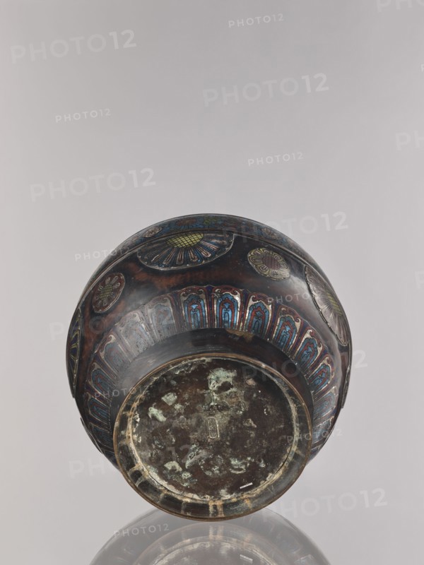 Flowerpot, Shimasa;, Japanese, Meiji period late 19th century, 1868–1912. Champlevé enamel on bronze; floral ornament. Jardinière vessel. Height 30.4 cm; diameter 41.2 cm., A rounded metal vessel photographed from below, showing the base and lower body with decorative panels; the surface is dark brown to black with areas of greenish corrosion on the base and accents of blue, red, yellow, and green in the ornamental designs, including floral and petal-like motifs, and a band of repeated arch-shaped patterns in blue and red around the body; the background is a pale gray and the vessel casts a faint reflection on the glossy surface beneath.