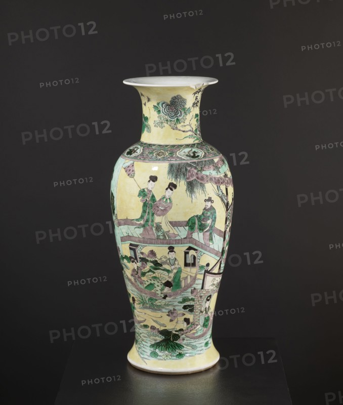 Vase, park scenes with architecture, enamel paints, Chinese art, Chinese culture, ceramics, decorative vessel, signed, 19th century, China, vessel, height 59.5 cm, diameter 25 cm, A tall ceramic vase with a flared rim sits against a dark background; the vase has a pale yellow base color with painted scenes in green, pink, purple, brown, and black, including a group of human figures wearing traditional clothing depicted around the body, architectural elements like railings and a small pavilion, stylized plants and lotus leaves at the lower section, decorative floral motifs near the neck, and delicate linework outlining faces and garments.