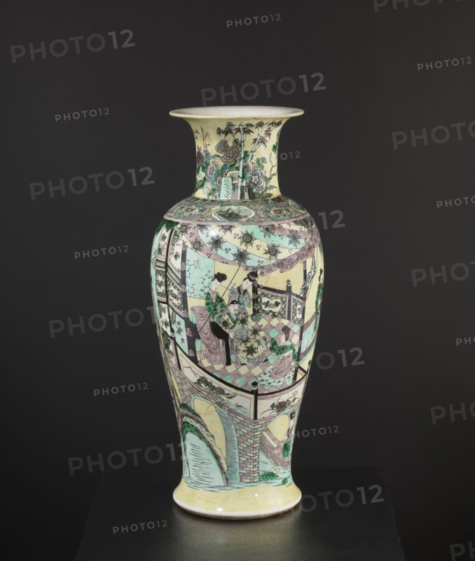 Vase, park scenes with architecture, enamel paints, Chinese art, Chinese culture, ceramics, decorative vessel, colored porcelain, 19th century, China, vessel, height 59.5 cm, diameter 25.5 cm, A tall porcelain vase with a flared rim and rounded shoulder standing on a short foot, decorated all over with painted scenes and patterns in pale yellow, mint green, soft pink, black, and white, with touches of darker green; the neck shows a garden scene with stylized trees and plants and a patterned band at the shoulder, the main body depicts a group of figures seated and standing on a tiled floor beneath draped cloths and decorative medallions, framed by architectural elements including railings and patterned panels, while the lower section features an arched bridge and water motif with brickwork and foliage; the overall surface combines delicate line work, floral motifs, and geometric borders, set against a dark neutral background.