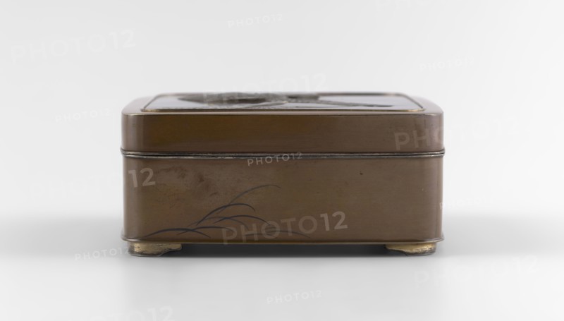 Box with a lid, Jômi, Eisuke I 1839-1899 artist; geese, grass; Rectangular box with rounded corners, decorated on the flat lid with two flying wild geese made in high relief with inlay of silver and gold iro-e zogan technique. The side walls are decorated with a motif of inclined reeds, made of silver and shakudo using the hira-zogan technique, i.e., the decorative motif is level with the background surface, giving a painted effect. On the lid there is a gold signature in a square field with two stylized kanji characters resembling archaic ones: Shobi. Ca. 1880–1899 Meiji Period, 1868–1912, Kyoto, Japan. Container. Height 4.8 cm; width 10.2 cm; depth 11.4 cm., A rectangular metal box with rounded corners sits on small curved feet, shown from the front against a pale background; the box is primarily brown with darker brown and black decorative lines suggesting a simple plant motif on the lower front panel, and there are thin metallic edges and a slightly darker band where the lid meets ...