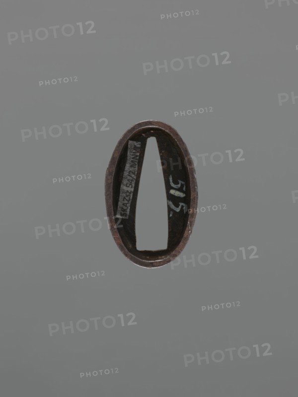Metal collar ending a sword hilt fuchi, decorated with a deer; Edo period 18th century, Japan, height 3.7 cm, width 2.3 cm, depth 1.2 cm., An oval metal object with a dark brown and rusty surface floats against a plain gray background, showing an inner hollow with a tapered rectangular opening and a few areas of darker patina and lighter worn edges, and a small patch of off-white marking visible inside.