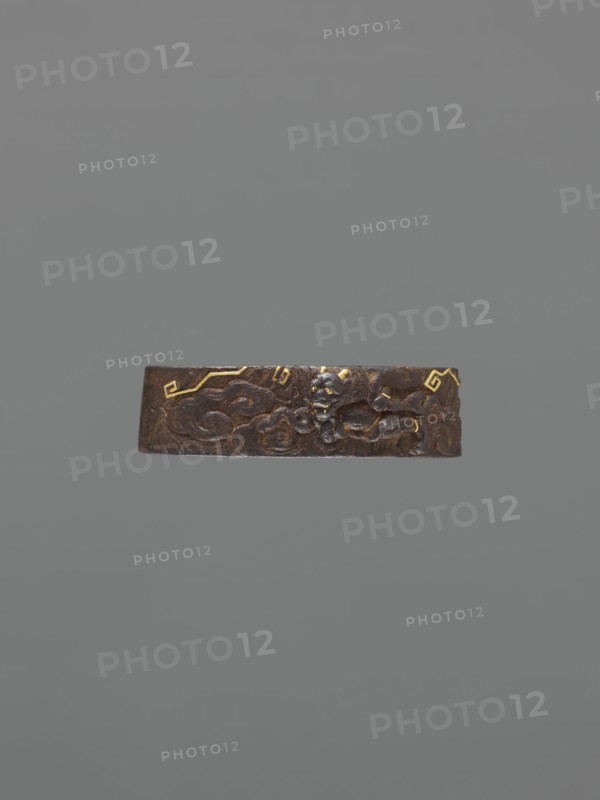Metal collar ending a sword hilt fuchi, Oni demons motif, Japanese, Edo period 1603–1868, 18th century, katana hilt fitting, materials: metal, dimensions: height 3.9 cm, width 2.3 cm, depth 1.1 cm., A horizontal brown metal band with a textured, carved surface sits against a plain gray background; the band shows a raised, sculpted design including a small carved face or mask and swirling cloud-like forms, and there are a few small gold accents on the band.