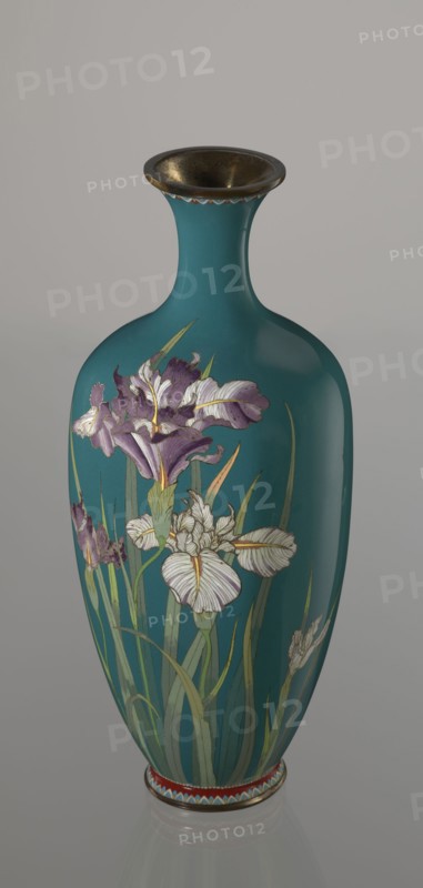 Vase, repossession Krakow, irises, flowers iconography, Meiji 1868–1912, Japanese art, cloisonné enamel, Japanese culture, Ovoid vase one of a pair, slender, on a low ring-shaped foot and with a narrow neck, flaring at the rim. The foot and mouth are framed with sheet metal. Decorated with a motif of a blooming iris bush, captured with naturalistic fidelity and attention to a variety of color tones. Executed using the yusen technique, the motif is placed against a uniform sea-green background. Around the foot and the rim there are narrow, colorful borders, also made using the yusen technique, composed of small triangular forms called cicada wings. ca. 1900 Meiji Period, 1868–1912, Nagoya, Japan. Vessel; height 25 cm, width 9.7 cm, depth 8.8 cm., A tall vase with a narrow neck and flared rim sits against a neutral background, its main body a teal color with a glossy finish, decorated with painted floral motifs showing a group of iris flowers in shades of purple and white with yellow acc...