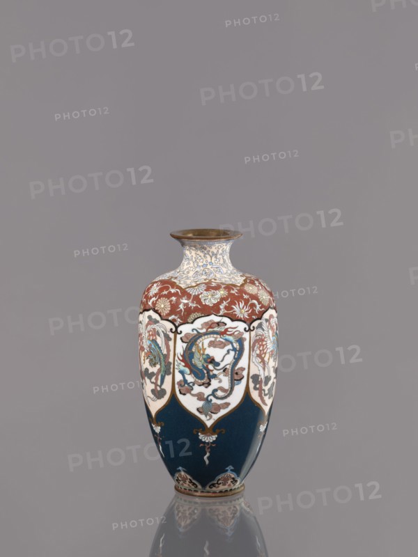 Vase, Cloisonné enamel vase on a small, ring-shaped foot, with a short neck ending in a spout widening toward the top. Decoration: stylized plant ornament; alternating dragon and phoenix hoo in six reserves; motifs include Japanese dragon and phoenix. Meiji period, ca. 1890–1900. Japan, Kyoto. Vessel. Height 15.0 cm; diameter 8.0 cm., A single ornate vase centered against a plain gray background, showing a bulbous body with a flared rim and a narrow neck; the rim appears metallic brown, the neck and upper shoulder have a cream base with intricate blue and gold floral-like patterns, the shoulder also includes a band of reddish-brown decorated with cream and gold floral motifs, a few scalloped white panels around the midsection contain multicolored decorative motifs in shades of blue, green, red, and brown, the lower body is a deep navy blue with small gold and cream embellishments near the base, and the vase rests on a reflective surface that mirrors its colors.