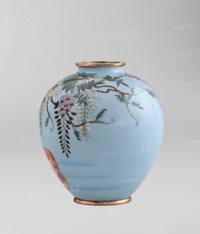 Vase by Gonda Hirosuke 1865–1937, cloisonné enamel, small spherical vase one of a pair on a low ring foot with a round ring spout, both set in silver-plated metal. Decorated with a realistic, colorful motif of red veil fish beneath hanging wisteria leaves and flowers on a light blue background. Bottom bears the enameller's mark: a flaming pearl with the katakana character ko Gonda Hirosuke of Nagoya. Circa 1890–1910 Meiji 23–43, Nagoya, Japan. Vessel; height 9.0 cm, diameter 8.2 cm., A smooth rounded vase with a pale blue background featuring a hanging floral design in shades of white, purple, dark green, and brown, with a few elongated leaf clusters and curved stems; the vase has metallic gold or bronze rims at the top and base and a small section of reddish-orange visible near the lower side.