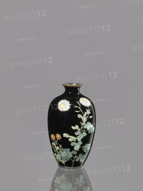 Vase, chrysanthemums, Japanese, flowers iconography, Meiji 1868–1912, cloisonné enamel, ovoid elongated vase, 19th/20th century Meiji period, Japan; vessel; height 9.0 cm, diameter 5.3 cm, A small black vase with a glossy finish sits centered against a gray background, showing a floral design of pale green stems and leaves with white and yellow daisy-like flowers and a few orange blossoms; the vase has a narrow neck with a metallic rim and a subtle reflection of the vase and floral motif visible on the surface beneath.
