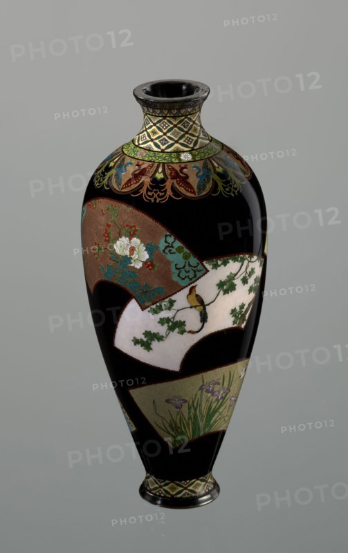 Vase by Namikawa Yasuyuki 1845–1927, ca. 1890–1905 Meiji period. A small, slender cloisonné enamel vase, height 18.0 cm, diameter 7.8 cm. The body tapers toward the bottom and terminates in a ring-shaped silver foot; the short neck is slightly parted at the spout and enclosed by a silver ring. An ornamental shippo motif border with rosettes in rhomboid fields encircles the foot and a similar border adorns the neck. From the neck a decoration of petals filled with stylized phoenix images flows down to the shoulders. The belly is covered with shiny black enamel and decorated with six colorful fan-shaped reserves showing various floral and bird motifs, executed with meticulous precision in the yusen technique using silver wires. A silver plaque mounted in the mirror of the bottom is engraved “Kyoto Namikawa.” Made in Kyoto, Japan., A tall, glossy vase with a narrow neck and flared rim sits against a neutral gray background; the vase has a predominantly black surface interrupted by several...