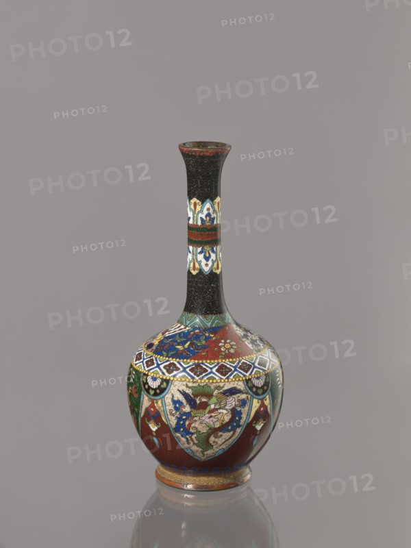Vase, Japanese, Meiji period 1868–1912, ca. 1900. Cloisonné enamel vessel decorated with birds, dragons, and phoenixes. Height 19.3 cm, width 8.9 cm., A narrow-necked vase with a bulbous body stands against a plain gray background, featuring a predominantly black neck with intricate small circular patterns and a decorative band of cream, blue, red, and green near the middle, while the rounded body displays rich areas of red, green, blue, cream, and gold in ornate floral and geometric motifs, accented with dark outlines and small touches of white, and the vase sits on a short foot ring showing bands of gold and reddish-brown.