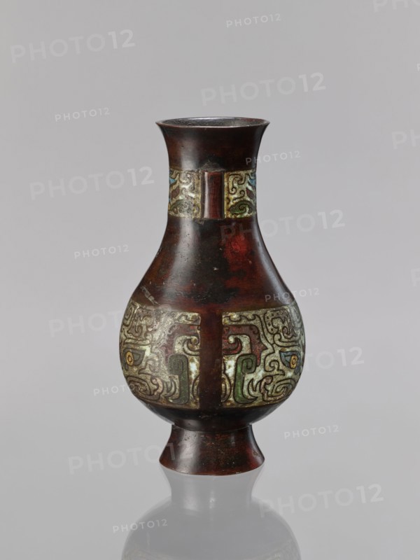 Vase, Chinese, taotie motif, Qing dynasty 1644–1911, 19th century, ceremonial/ritual vessel, porcelain/ceramic vessel, height 24 cm, diameter 13.1 cm, China place of origin uncertain, A single vase with a flared rim and a narrow neck widening into a bulbous body above a flared foot, shown against a plain light gray background; the vase surface is primarily dark brown with reddish undertones and a glossy patina, and it bears a band of ornate raised decoration around the midsection and another narrower band near the neck featuring swirling abstract motifs in muted green, pale yellow, light blue, and olive hues set against a lighter, aged background; the upper rim and lower foot remain the dark brown color, and the vase casts a soft reflection on the surface below.