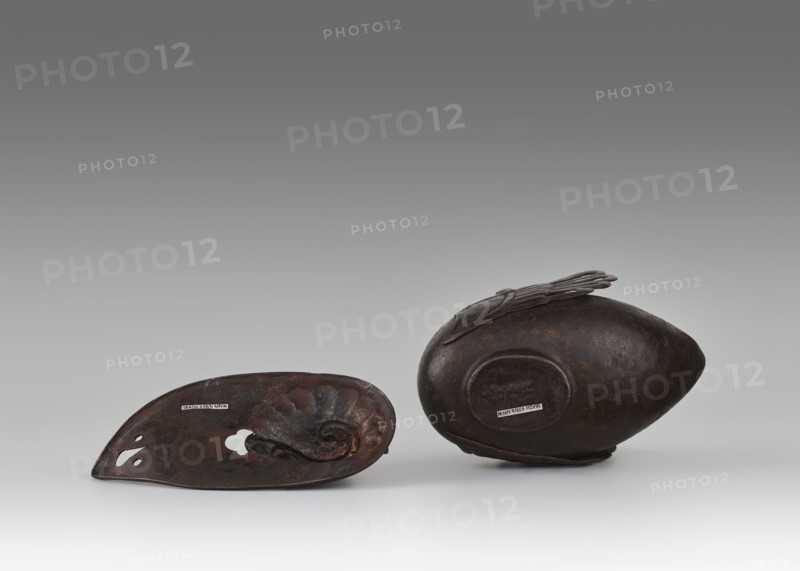 Duck incense burner, Chinese, Qing dynasty 1644–1911, 19th century. Ceramic vessel in the form of a duck with wings, used as an incense burner; height 9.7 cm, width 13.6 cm. Subjects: ducks/birds. Provenance unknown., A group of two dark brown metal objects rests on a light gray surface against a gradient gray background, one object lying on its side with an oval, slightly pointed shape and a raised circular area on its side, and the other object shown interior-side up with a concave form, organic curved ridges, and a few cutout shapes; the colors visible include dark brown, rust tones, and shades of gray.