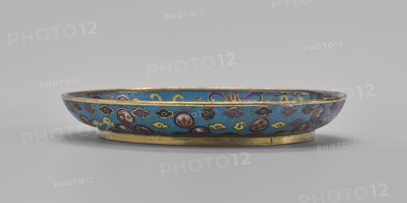 Plate, Chinese, Qing dynasty 1644–1911, cloisonné enamel, 19th century. Round plate with a flat bottom, without a distinct facet, with an arched rim on a low foot arranged in a ring at the rim; height 2 cm, diameter 14.7 cm. The mirror is decorated with a tondo surrounded by a multicolored lotus tendril. The composition in the tondo depicts a cricket in motion perching on a flowering plant jumping from one flower to another, the insect located on the left side; flowering plants dominate the image. The outer rim is filled with medallions depicting stylized Chinese symbols lotus, peach, surrounded by free-form cloud projections. The underside of the bottom is covered with single-color turquoise enamel., A shallow round dish sits on a low circular foot, showing a bright turquoise interior and exterior background decorated with a repeating pattern of round medallions and cloudlike motifs in colors including deep blue, dark red, yellow, purple, white, and black, with metallic gold edging ar...