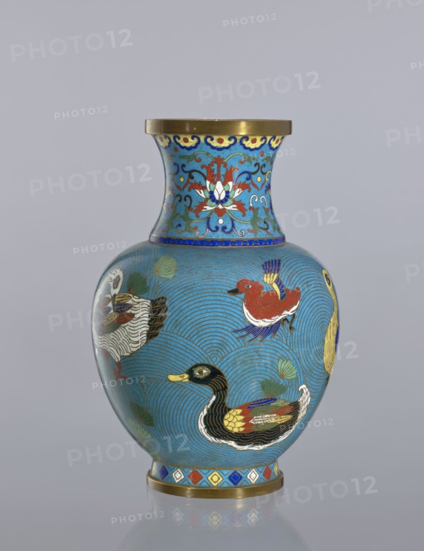 Vase, : Paderewski, Ignacy Jan 1860–1941. Chinese art; Chinese; Qing dynasty 1644–1911. Cloisonné enamel decorative vessel vase on a foot with a neck. Decoration: ducks on a turquoise background; lotus tendril on the neck. 19th century. China. Height: 23.5 cm., A rounded vase with a narrow neck and flared rim sits against a plain pale gray background, decorated in bright colors on a predominantly turquoise-blue ground; the neck features stylized floral motifs in red, white, green, dark blue, and gold with a gold rim at the top, while the body shows a pattern of concentric wave-like lines in darker blue and several painted ducks in colors including black, yellow, red, white, green, and blue, along with green leaf shapes; a decorative band with diamond shapes in red, blue, yellow, white, and gold encircles the base, which also has a gold edge.