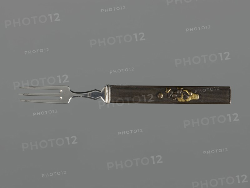 Fork with knife handle kozuka, Japanese, Edo period 1603–1868, 18th century; katana kozuka knife/handle used with swords, fork; cutlery; height 16.9 cm, width 1.4 cm., A metal fork with a long rectangular handle lies horizontally against a gray background, the fork tine section on the left and the handle on the right; the tines and neck are silver and reflective with a smooth polished finish, transitioning to a dark brown handle that has a fine textured surface and a narrow silver collar where it meets the metal; the handle features a small raised decorative motif in golden and darker metallic tones near its mid to right portion.