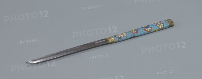 Travel cutlery set in case; Chinese, Qing dynasty 1644–1911, 19th century. Includes: a Knife with a cloisonné enamel handle and steel blade; b–c Ivory chopsticks decorated with an inlaid black lacquer ornament at the top in the form of a border; d File decorated similarly to the chopsticks; e Cloisonné enamel case reaching 3/4 the height of the cutlery, with bronze fittings engraved with ornamentation at top and bottom, interior lined with wood. Chopsticks and file are held by a band decorated with a matching border; a narrow cotton-silk strap with fringes is attached. Case decorated with flowers in two reserves and plant tendrils in the background. Motifs include plant designs and a swastika. Function: travel cutlery. Length: 28 cm case., A long metal blade with a pointed tip lies diagonally on a gray background, attached to a cylindrical handle decorated in light blue with floral patterns in red, white, yellow, and dark blue, and accented with metallic gold-colored bands at the blade...