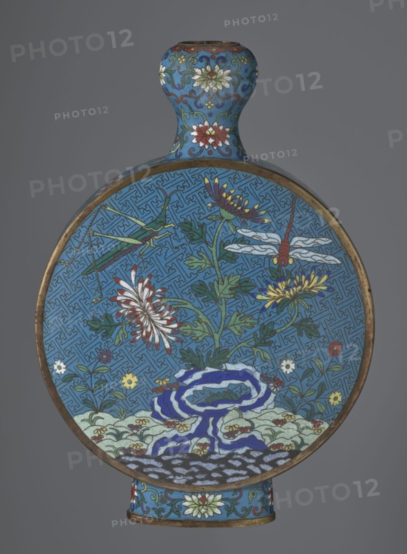 Vase - moon bottle pilgrim bottle with a flattened belly, supported by a separate oval high foot, with a short neck resembling a garlic bulb suantoukou type. Decoration on one side: a multicolored composition depicting a chrysanthemum flower growing on a coastal rock, above which a dragonfly and a grasshopper hover. The other side shows lilies irises on a rock above the water, with a butterfly and a grasshopper above them. Small, colorful shore flowers appear in both representations. Both compositions use the flowers and birds motif known from Chinese scroll painting. A Chinese meander forms the background for both compositions. The foot, side edges, and neck are filled with a lotus tendril. Colors dominated by red, white, green, yellow, and navy blue. Elements without enamel decoration are gilded; there are visible abrasions of the gilding and firing-related technological defects. Cloisonné enamel. Qing dynasty 2nd half 18th century. China. Vessel. Height 29.8 cm, width 21.1 cm., A ro...
