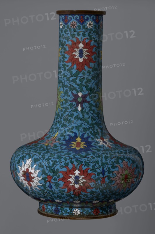 Vase, gift, Chinese, Qing dynasty 1644–1911, cloisonné enamel with lotus and lotus tendril ornament. Vase with a long, wide neck, supported on a separate ring-shaped foot, with a flattened spherical belly, the main decoration a dense, multicolored lotus tendril surrounding the entire surface. Foot decorated with an ornamental band of small flowers and leaves. Upper edge of the neck at the rim decorated with a border of ruyi-heads. Neck ends with a thick, ungilded metal ring. 2nd half of the 18th century, China. Vessel; height 37.8 cm, diameter 15.5 cm., A tall, bulbous vase with a long narrow neck sits against a gray background, covered in an intricate floral pattern on a turquoise-blue field; the design features large stylized flowers in red, white, yellow, blue, purple, and green, surrounded by curling dark green vine-like motifs and small decorative floral borders, with a dark brown rim at the top and a slightly flared base rim showing additional small flower motifs.