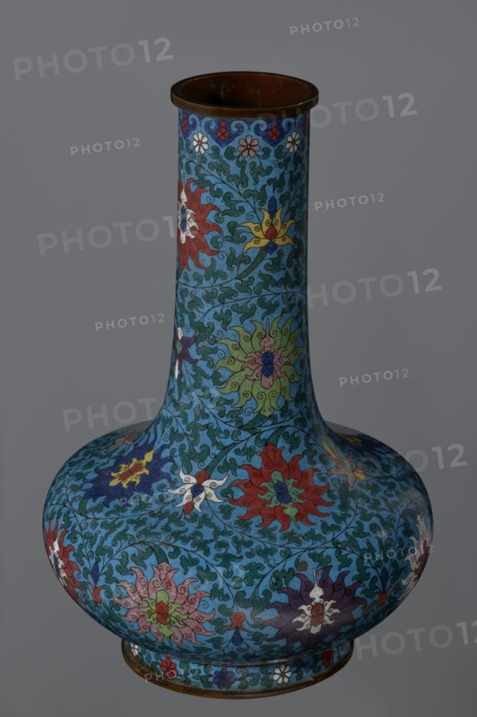 Vase, Chinese, Qing dynasty 2nd half of the 18th century. Cloisonné enamel vessel with a long, wide neck, supported on a separate ring-shaped foot and with a flattened spherical belly. Main decoration: dense, multi-colored lotus tendril surrounding the entire surface. Foot decorated with an ornamental band of small flowers and leaves. Upper edge of the neck at the rim decorated with a border of ruyi-heads. Neck ends with a thick, ungilded metal ring. Height 37.8 cm; diameter 15.5 cm., A single tall vase with a bulbous base and narrow neck occupies the image, covered in an intricate floral and foliate pattern on a predominantly blue background; the surface shows stylized flowers and swirling leaves in colors including red, green, yellow, white, purple, and dark blue, with darker outlines defining the motifs and a metallic dark bronze rim and base edge.