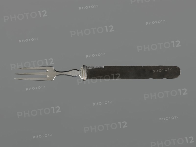 Fork with knife handle kozuka, Japanese, Edo period 1603–1868, 18th century; materials: metal cutlery; subject/iconography: dragons and fish; function: kozuka knife handle for a katana; dimensions: height 16.8 cm, width 1.4 cm; melee weapon accessory., A metal fork with three tines and a silver-colored neck is shown horizontally against a neutral gray background, the handle extending to the right and appearing dark brown to nearly black with a textured, scalloped edge. The fork's metal portion has a reflective silver tone with some darker spots and slight surface wear, while the handle is matte and richly dark, creating contrast with the silver. The overall composition is centered and minimal, featuring the contrasting silver and dark brown or black colors on a gray backdrop.