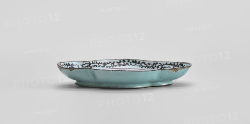 Plate, Chinese, Qing 1644–1911, 18th century, painted enamel depicting genre scenes, vessel; height 1.3 cm, width 7.5 cm, depth 9.1 cm., A shallow, oval dish with a scalloped rim glazed in pale turquoise on the exterior and interior, showing a decorative dark pattern along the inner rim; the rim and foot have darker brown edging and small areas where the glaze is worn or chipped, revealing a warmer, yellowish-brown beneath; the dish sits on a short circular foot and is photographed against a light gray background.