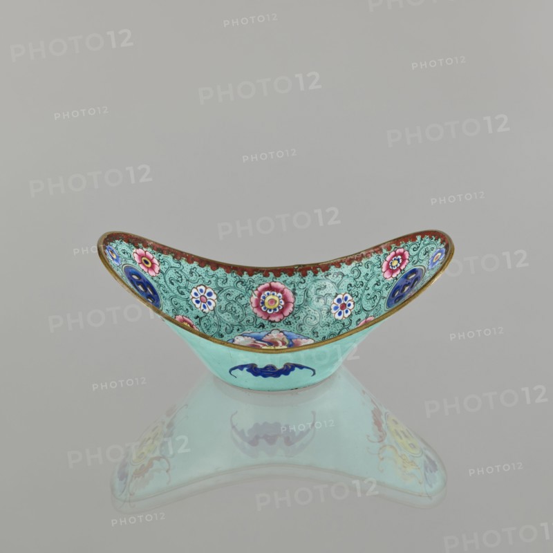 Bowl, painted enamel, Qing 1644–1911, Chinese, 18th/19th century. Ceramic vessel decorated with lotuses, coins, flower tendrils and bats iconography symbolizing happiness. Height 6.3 cm; width 8.5 cm; depth 15.3 cm., An ornamental bowl with a curved, crescent shape sits on a reflective surface, showing a mirrored underside; the bowl's exterior is a light turquoise with a dark blue stylized motif, while the interior features a detailed patterned background in turquoise with ornate swirls and a border in brownish-red, decorated with floral medallions in pink, white, blue, and yellow, and additional circular accents in deep blue and purple, all outlined with thin gold edging.