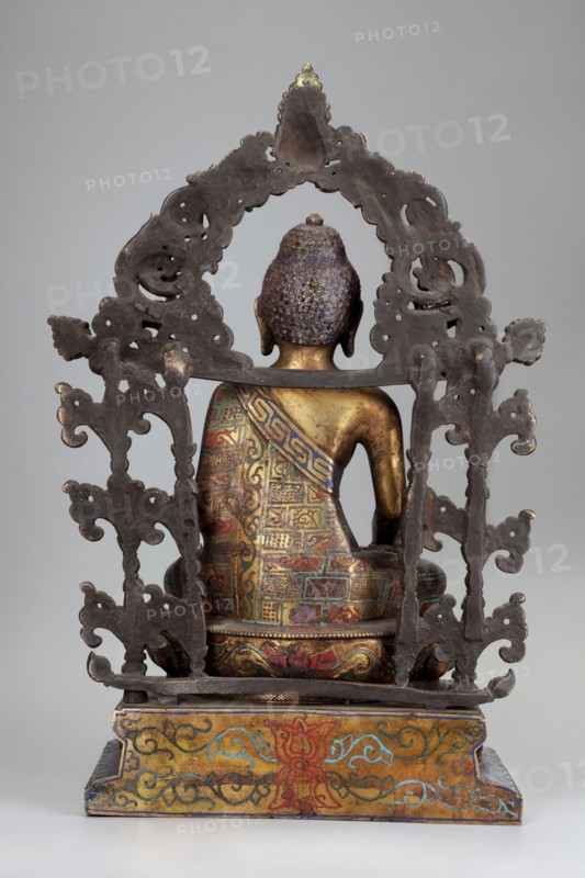 Shakyamuni Buddha, gift, Chinese, Himalayan/Tibetan Buddhist art, Sino-Tibetan style, Buddha iconography with bowls, lotus throne, ushnisha, vajras; 18th century, China; sculpture; height 38.0 cm, width 25.0 cm, depth 13.7 cm., A seated metal figure viewed from the back with a textured purple head and a golden neck and shoulders, wearing a colorful patterned garment in shades of blue, red, green, and gold; the figure sits on a decorated base with gold, red, blue, and green motifs, and is framed by an ornate dark metal arch with intricate cutouts and scroll-like shapes against a neutral gray background.