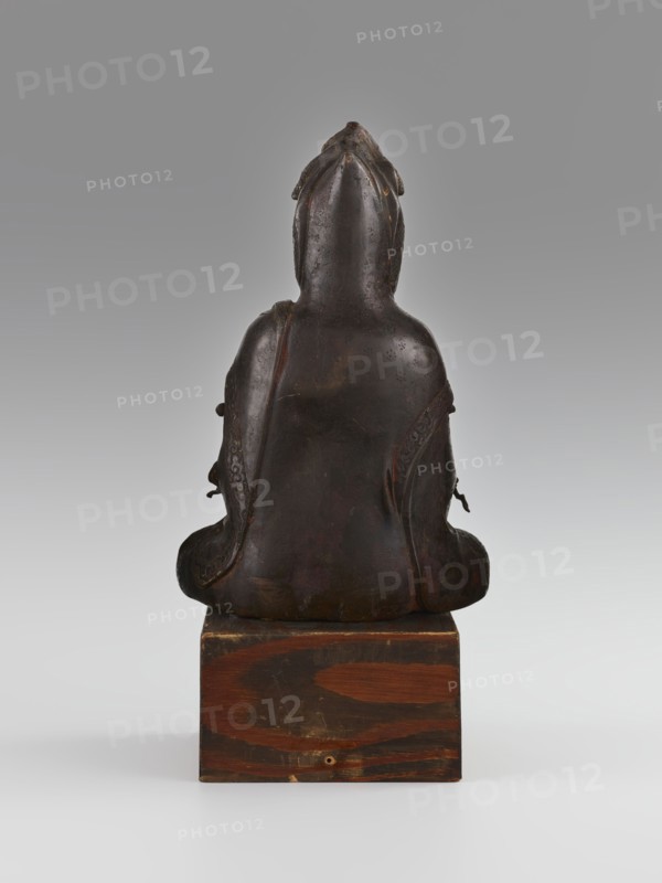 Guanyin, Avalokiteshvara iconography, Chinese Buddhism, Chinese art, Chinese culture, goddesses, bodhisattva iconography, mercy, 16th–17th century, China, sculpture, figurine, height 28.0 cm, A dark brown seated figure viewed from behind, with a smooth rounded back and a hooded head that tapers to a point at the top; the figure sits on a rectangular wooden block with visible wood grain in reddish-brown and darker brown tones, and the background is a gradient of light gray to darker gray.