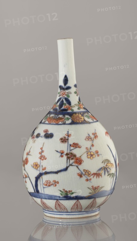 Bottle, porcelain, Arita, Japan, ca. 1700–1730; height 22.3 cm, diameter 12.2 cm. Decoration: Imari palette with bamboos, pines, plums Three Friends of Winter, sake motif; subject and plant ornament; Japanese ceramics., A rounded porcelain bottle with a long narrow neck sits against a neutral gray background; the bottle is primarily white with visible fine crackle in the glaze and decorated with hand-painted floral and botanical motifs in blue, orange, green, gold, and red; the shoulder and neck feature stylized floral bands in deep blue and orange with green leaves, while the body shows branches with blossoms in orange and red, leaves in green and gold highlights, and a blue horizontal band near the base; the foot has repeated leaf-like patterns in red and thin blue decorative bands.