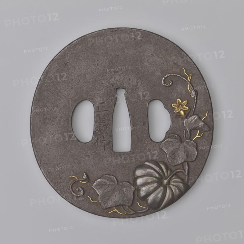 Crossguard tsuba, Masayoshi. Round tsuba maru gata with a rectangular edge kaku mimi, decorated on both sides with an asymmetrically composed high relief—carved takabori and inlaid with copper and gold takazôgan—depicting a plump pumpkin fruit with decoratively twisting stems, leaves and flowers. Details made with gold inlay using the nunome technique. Signed. 1st half of the 19th century Edo period, 1603–1868. Japan, Inaba historical province. Materials/subjects: metals, Japanese art; motifs include pumpkins, buffalo zodiac, plants. Tsuba; height 8.0 cm, width 8.35 cm, depth 0.45 cm., A round dark gray metal disk with three irregular central openings, decorated with a carved pumpkin and leaves near the lower right edge, a small flower and curling vine above the pumpkin, and thin winding vine accents; the carved elements include highlights in metallic silver and small accents in metallic gold, and the background surface is a textured matte gray.