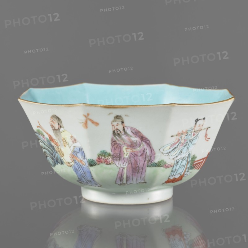 Bowl. Spherical bowl on a ring foot. Porcelain body with turquoise and transparent white glaze. Decoration painted with enamel paints and iron red depicting the Eight Immortals iconography. Colored porcelain, Qing dynasty, Jiaqing period 1796–1820, 18th/19th century China. Height 8.1 cm; diameter 17.6 cm; weight 0.4 kg.,  noted., A shallow porcelain bowl with a scalloped rim and a pale blue interior, edged in gold, sits against a neutral gray background; the exterior shows a painted scene of a group of figures wearing flowing robes in colors including purple, light blue, pale yellow, and white, with details in green, pink, orange, and red, set above a green ground with foliage and floral elements, and the bowl casts a faint reflection on the surface beneath it.